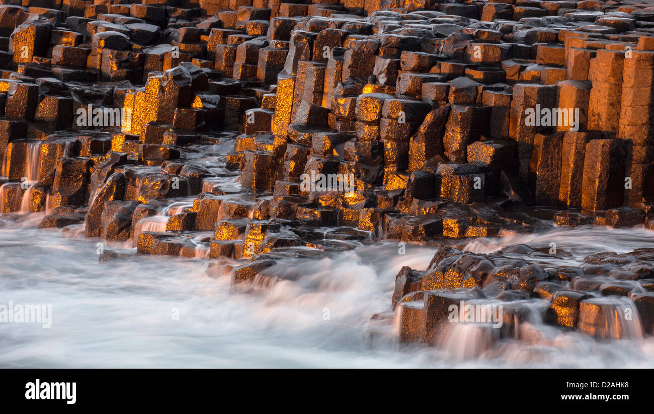Drammatica nel tardo pomeriggio la luce e spruzzi delle onde sulle rocce basaltiche da Il Selciato del gigante - punto di riferimento dell'Irlanda del Nord Foto Stock