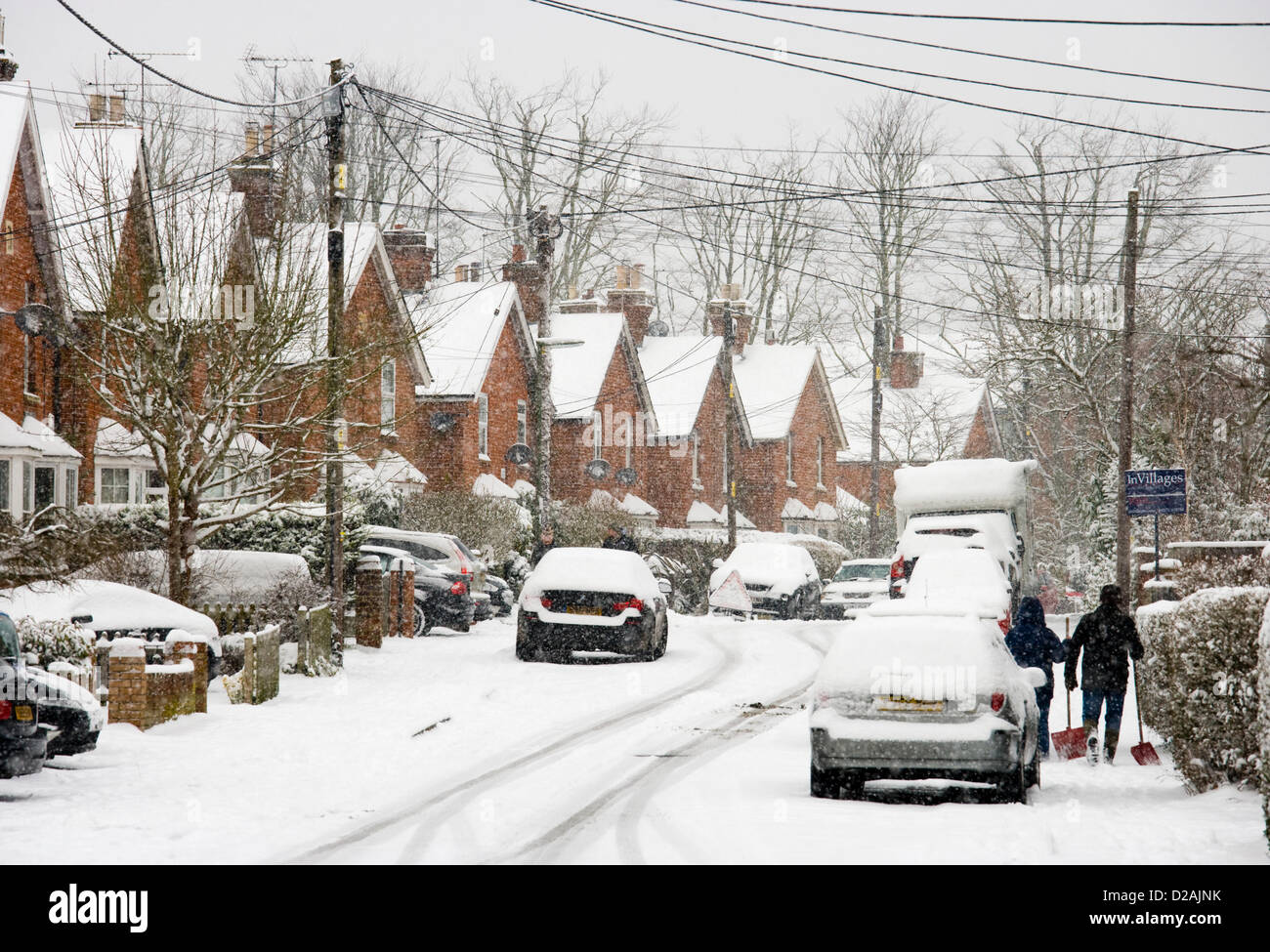 Persone con pale da neve in strada residenziale sotto la neve, Chobham, Surrey, Regno Unito. Foto Stock
