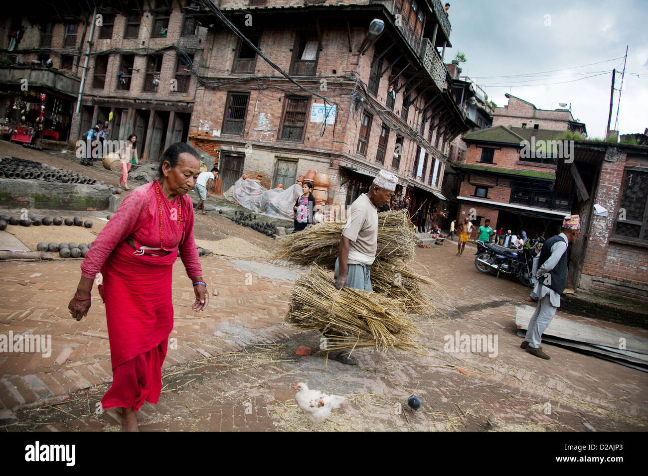 Un uomo cammina di fretta per ottenere la Sua paglia e pentole all'interno prima che la pioggia arriva a Bhaktapur. Il vasellame è un'industria tradizionale. Foto Stock