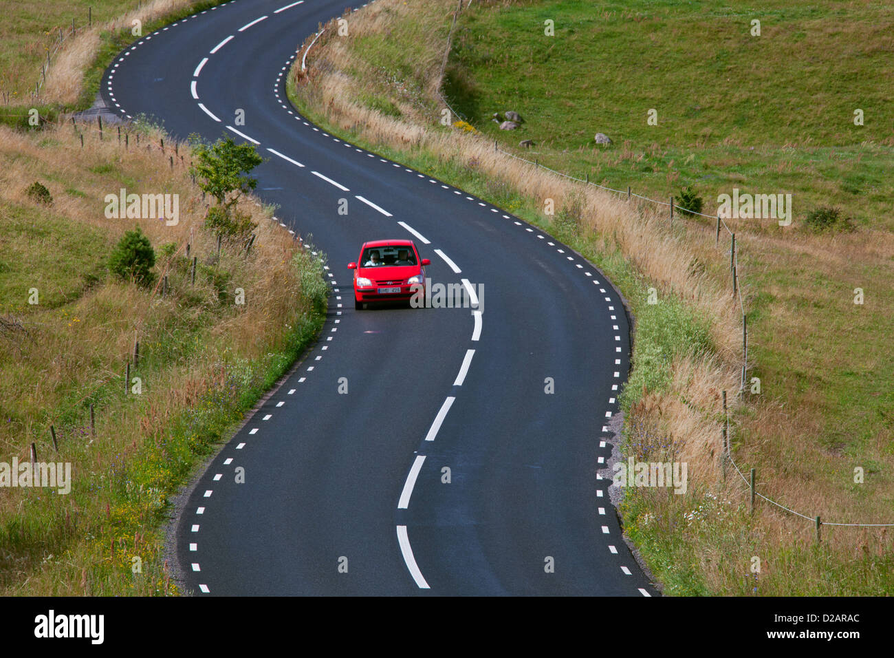 Rosso auto guidando lungo la tortuosa strada tra i campi a Brösar backar / Broesarp colline, Haväng, Skåne, Svezia Foto Stock