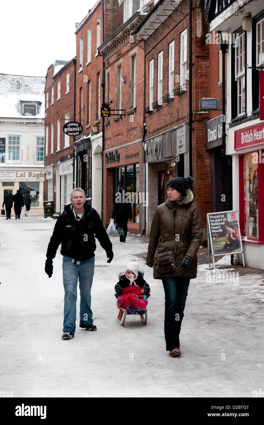 L uomo e la donna con il traino della slitta bambino sulla neve in Market Street Lichfield Staffordshire, Regno Unito Sabato 19 Gennaio 2013 Foto Stock