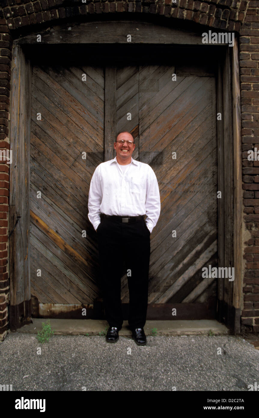 Ritratto 36 Anno Vecchio Uomo sorridente e in piedi di fronte a porte in legno Foto Stock