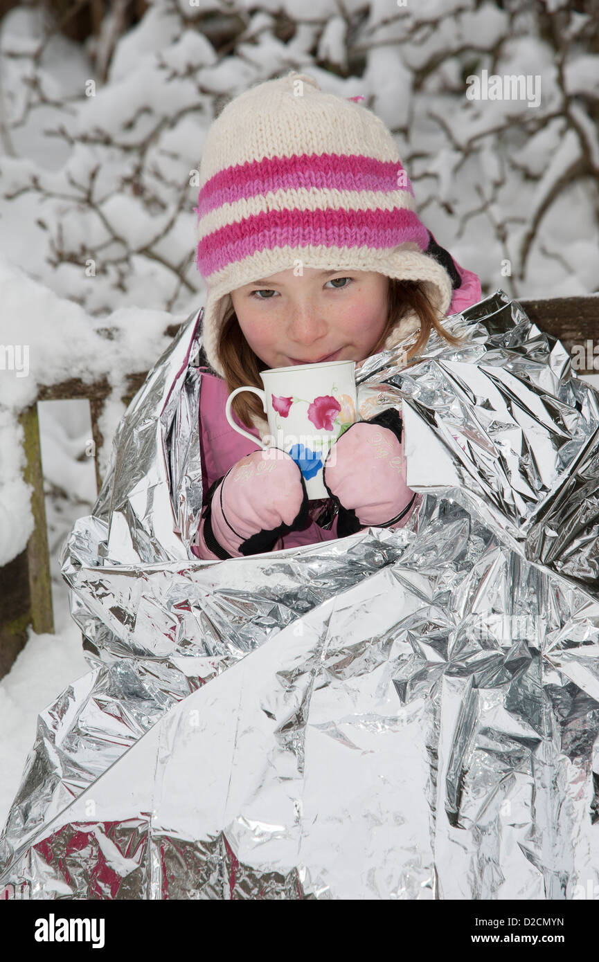 Ragazza giovane con una lamina coperta per trattenere il calore e di tenere fuori il freddo inverno gustando una bevanda calda Foto Stock