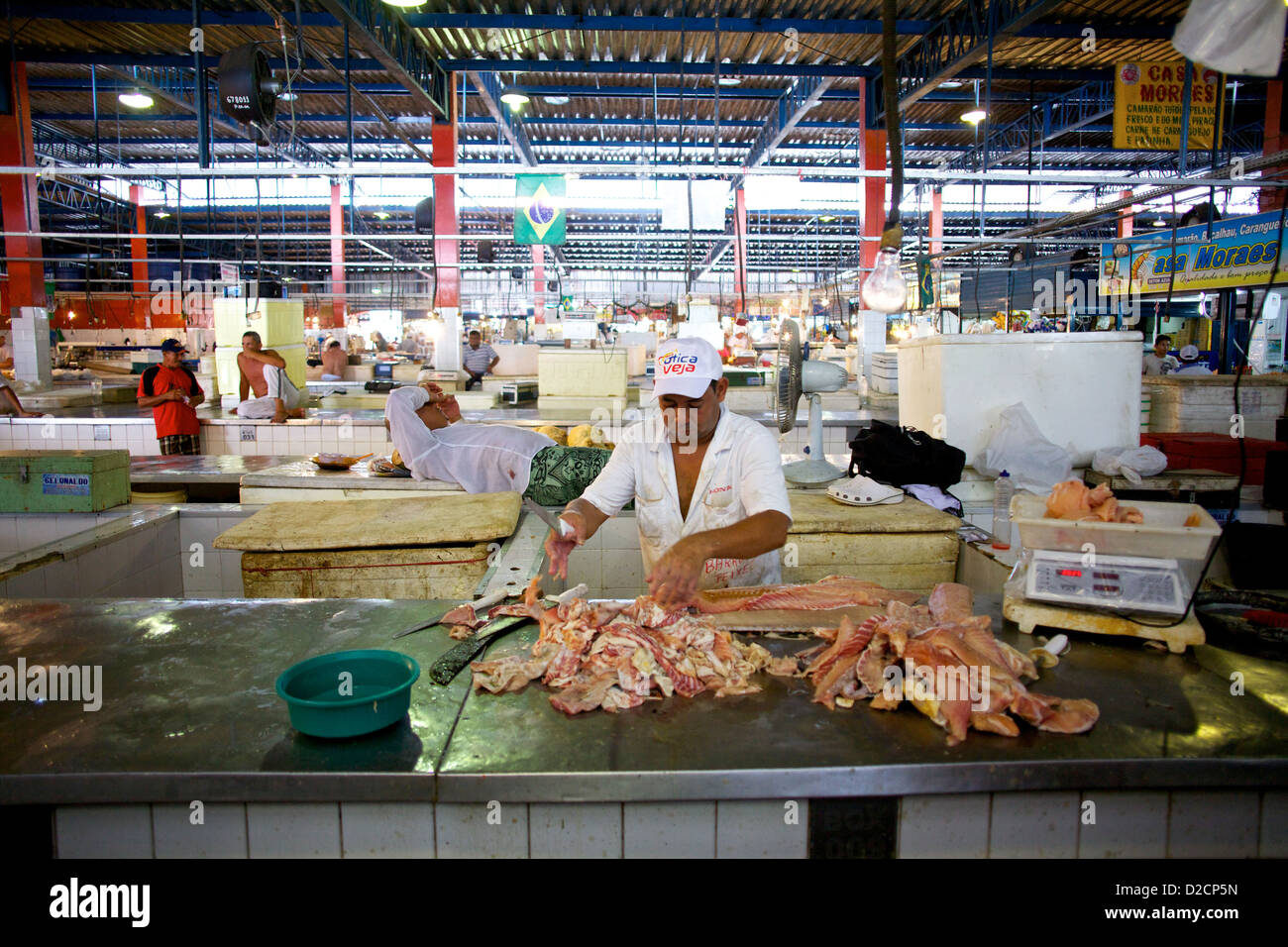 Un venditore di pesce che sfilettatura abilmente pesce fresco nel vivace mercato municipale Adolpho Lisboa a Manaus, Brasile, circondato da una vivace attività di mercato Foto Stock