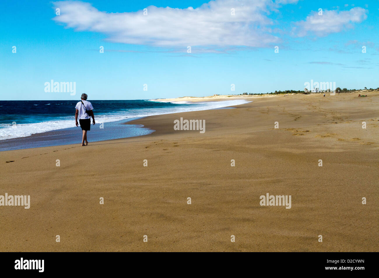 L'uomo portare una fotocamera passeggiate su di una spiaggia appartata vicino a Todos Santos, Messico Foto Stock