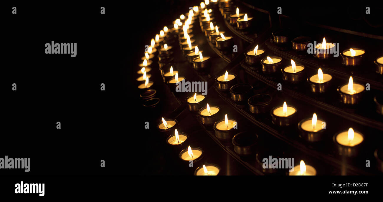 Molti acceso candele votive in una fila contro uno sfondo nero Foto Stock