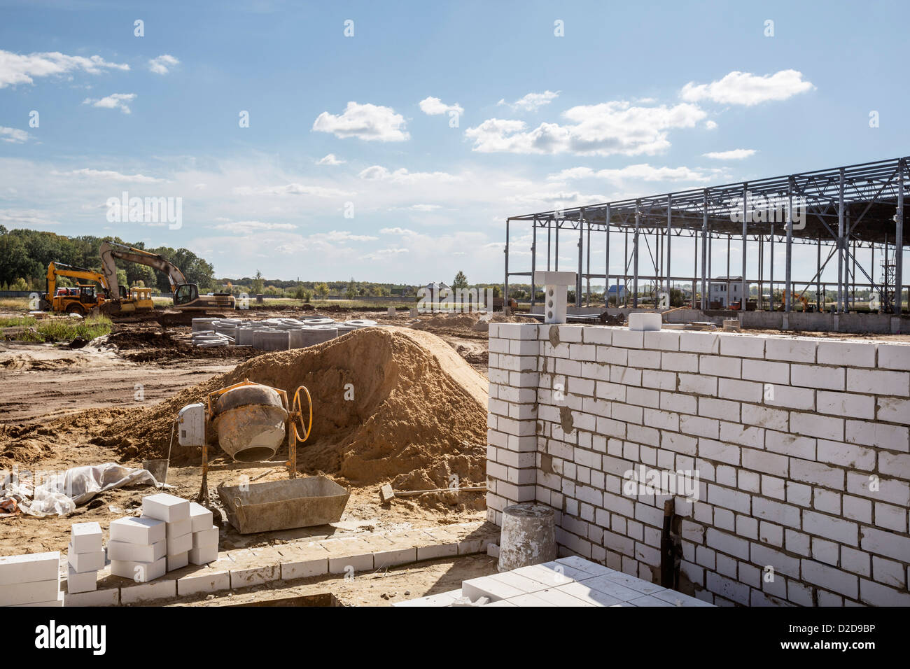 Un mescolatore di cemento e un muro di mattoni nella parte anteriore di un telaio di costruzione in corrispondenza di un sito in costruzione Foto Stock