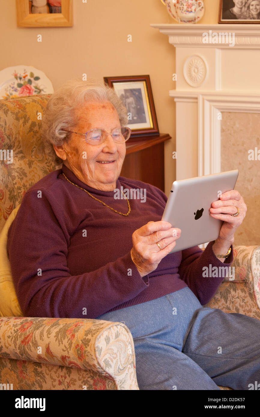 Donna anziana pensionata con gli occhiali su ipad apple tablet a casa rilassarsi sulla sedia la riproduzione di giochi per computer Foto Stock