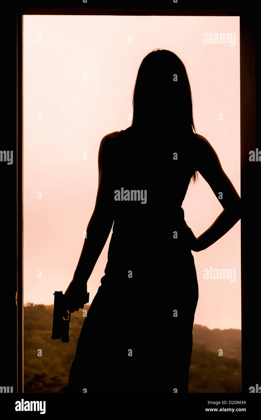 Silhouette di una donna in possesso di una pistola mentre in piedi in un telaio della porta. Foto Stock