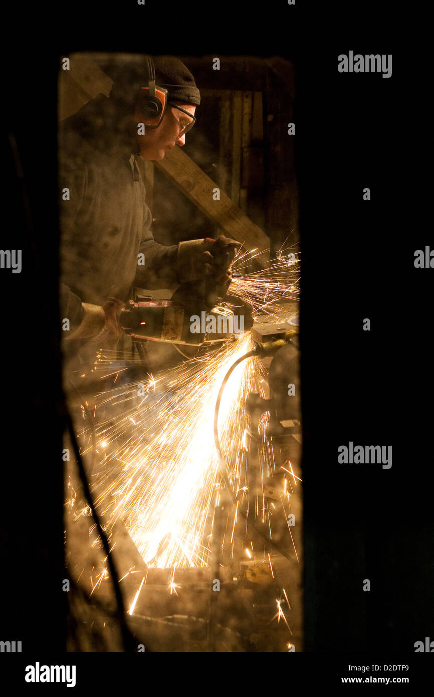 Immagine di un uomo preso attraverso una finestra di lui usando il disco elettrico mola di taglio creando un sacco di scintille da red hot metal. Foto Stock