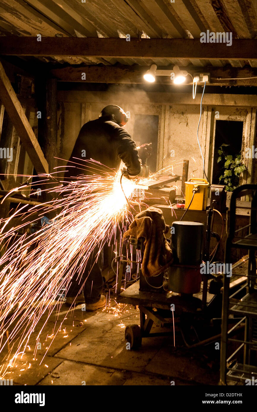 Un uomo con disco elettrico mola di taglio metallo tagli la creazione di partite di scintille, rosso metallo caldo mosche ovunque. Foto Stock