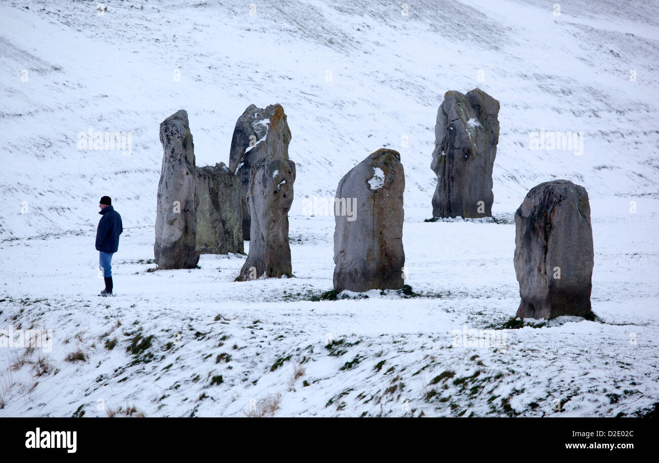 Uomo che cammina dalle pietre permanente ad Avebury nella neve Foto Stock