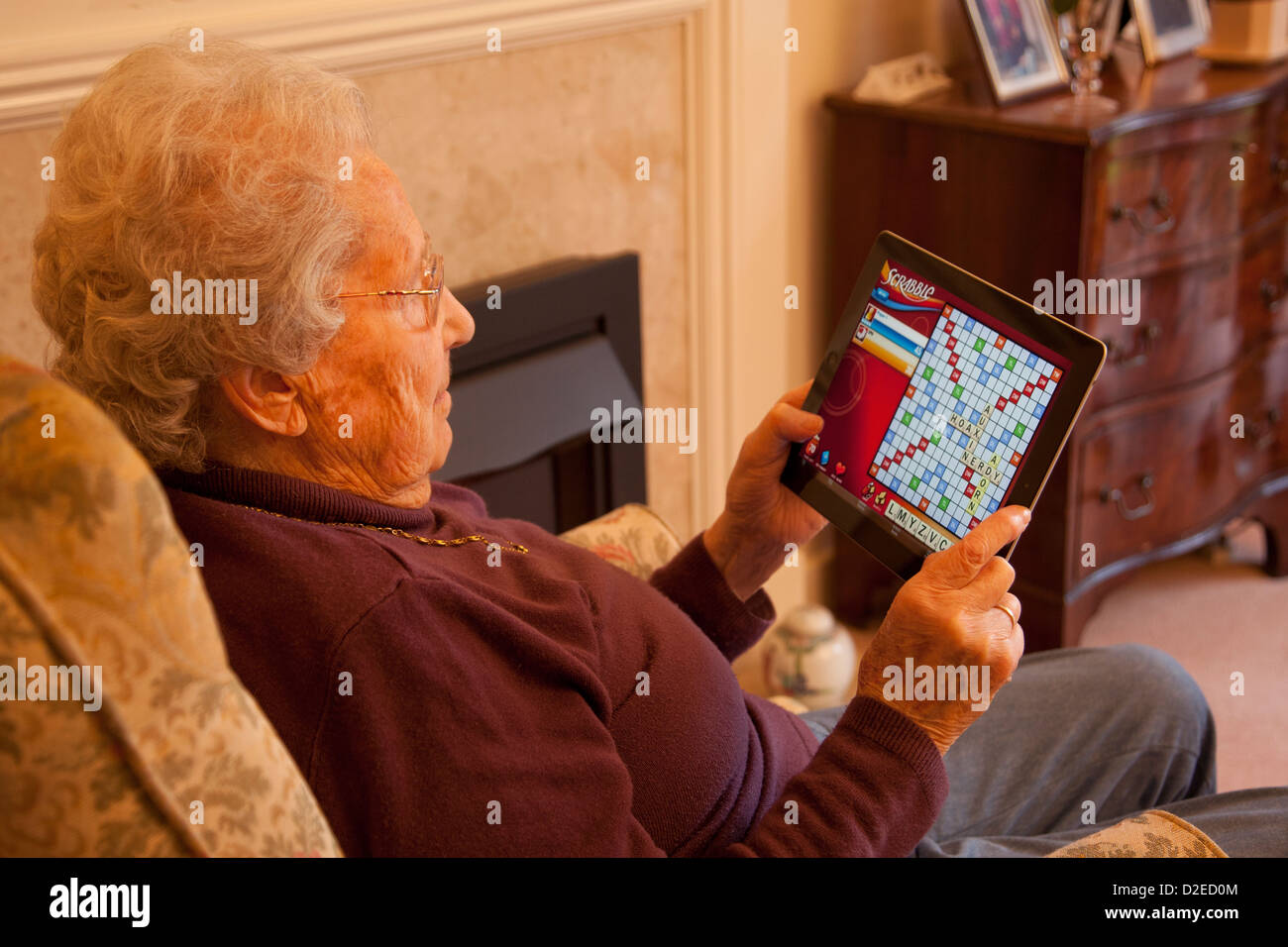 Donna anziana pensionata con gli occhiali su ipad apple tablet a casa rilassarsi sulla sedia a giocare a scrabble gioco per computer Foto Stock