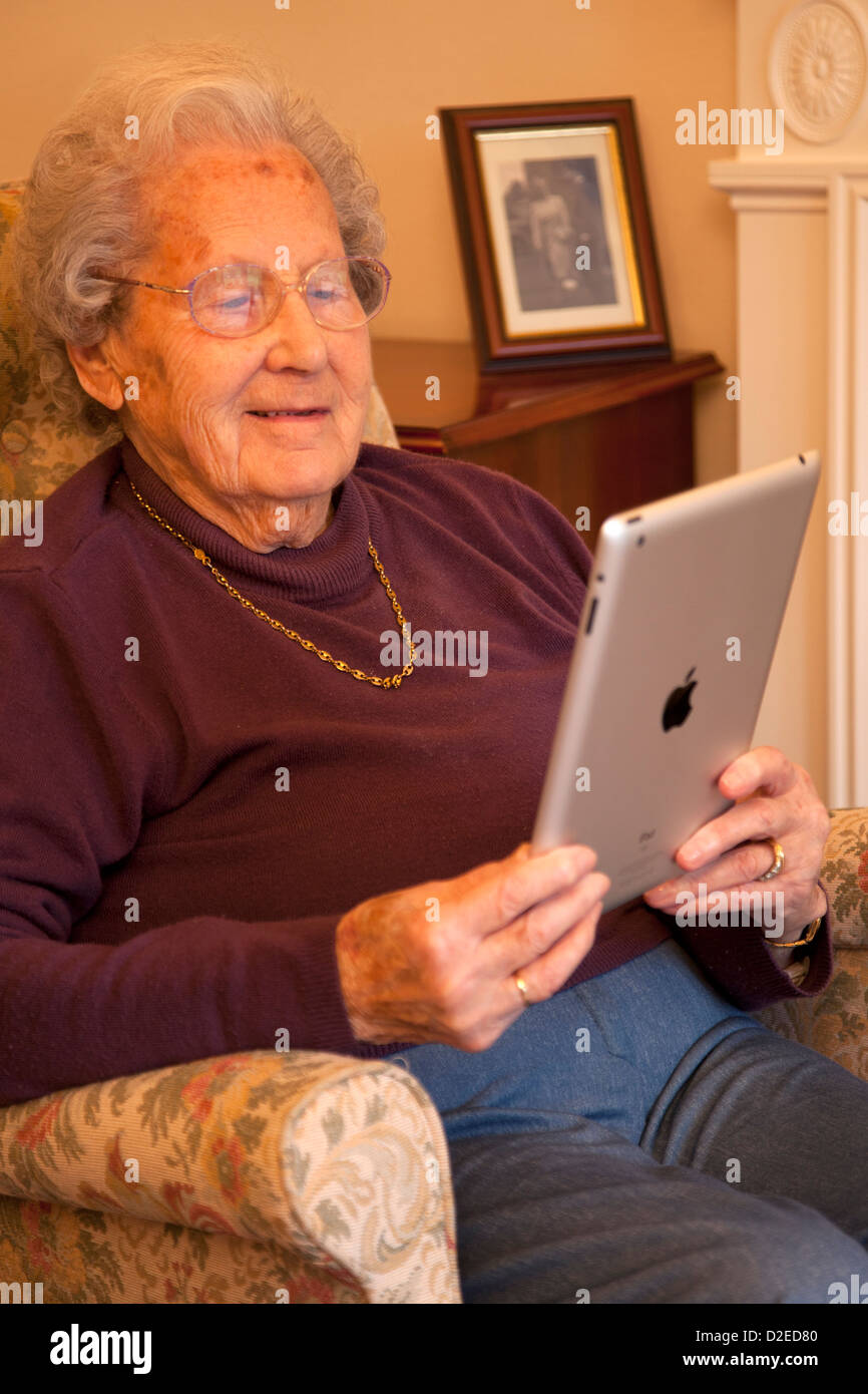 Donna anziana pensionata con gli occhiali su ipad apple tablet a casa rilassarsi sulla sedia la lettura di un libro Foto Stock