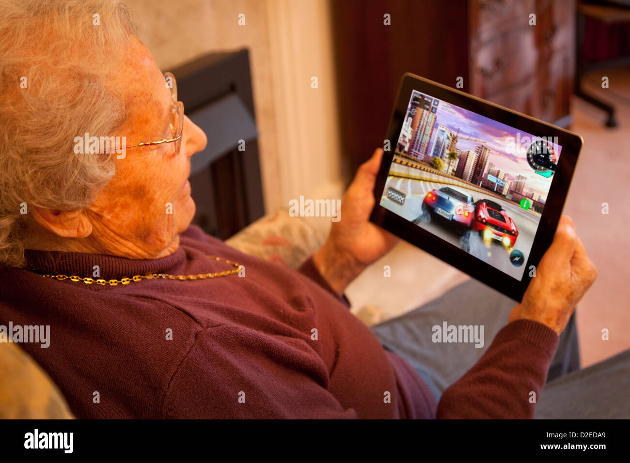 Donna anziana pensionata con gli occhiali su ipad apple tablet a casa e la riproduzione di un auto da corsa gioco per computer Foto Stock