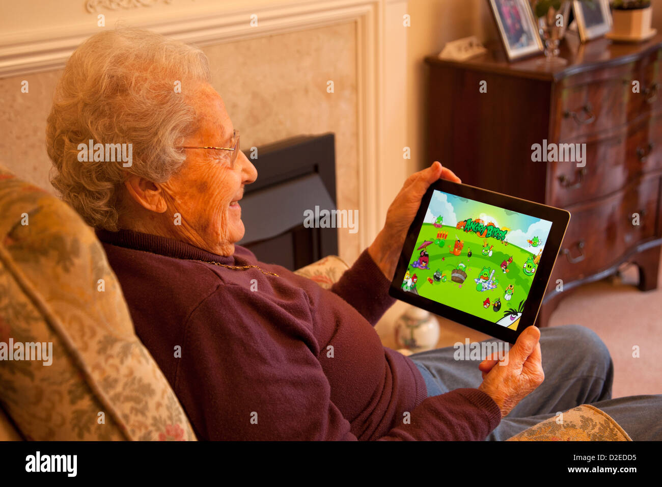 Donna anziana pensionata con gli occhiali su ipad apple tablet a casa rilassarsi sulla sedia giocando angry birds giochi per computer Foto Stock