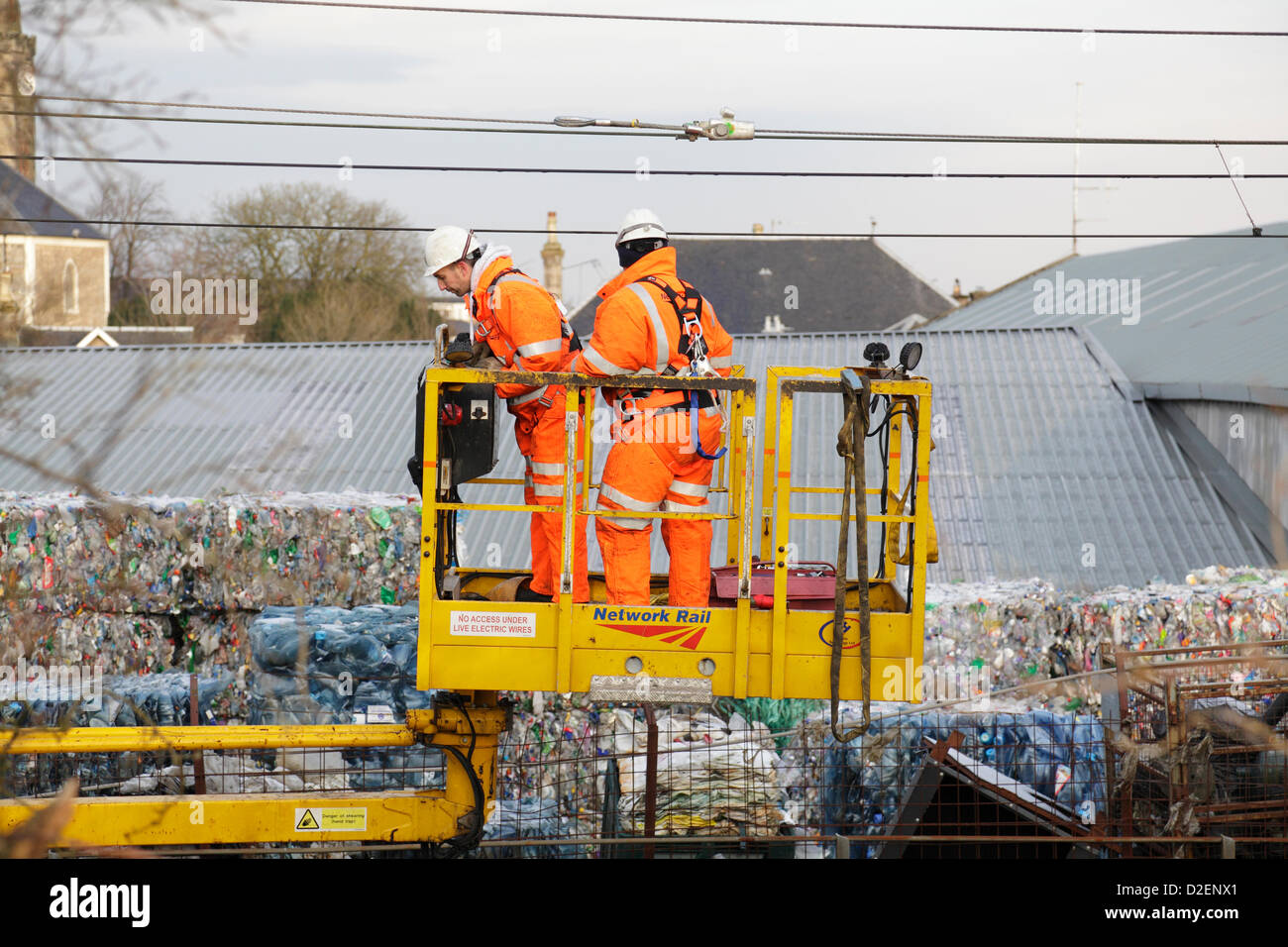 Johnstone, Renfrewshire, Scozia, Regno Unito, martedì, 22 gennaio 2013. I tecnici delle ferrovie di rete che ispezionano i cavi di alimentazione sospesi per verificare la presenza di danni in seguito a un incendio nell'impianto di riciclaggio WRC, che può essere visto in background, causando cancellazioni, ritardi e revisioni dei servizi di formazione sulla linea tra la stazione centrale di Glasgow e Ayr Foto Stock