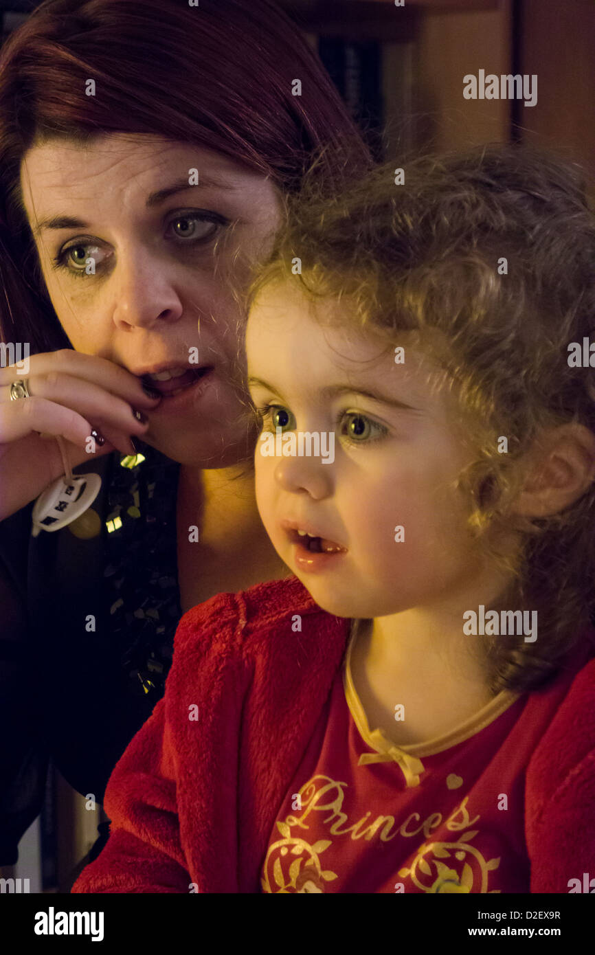 A due anni di bambina guardando una sbalorditiva rappresentazione dell arrivo di Babbo Natale in televisione con sua madre Foto Stock