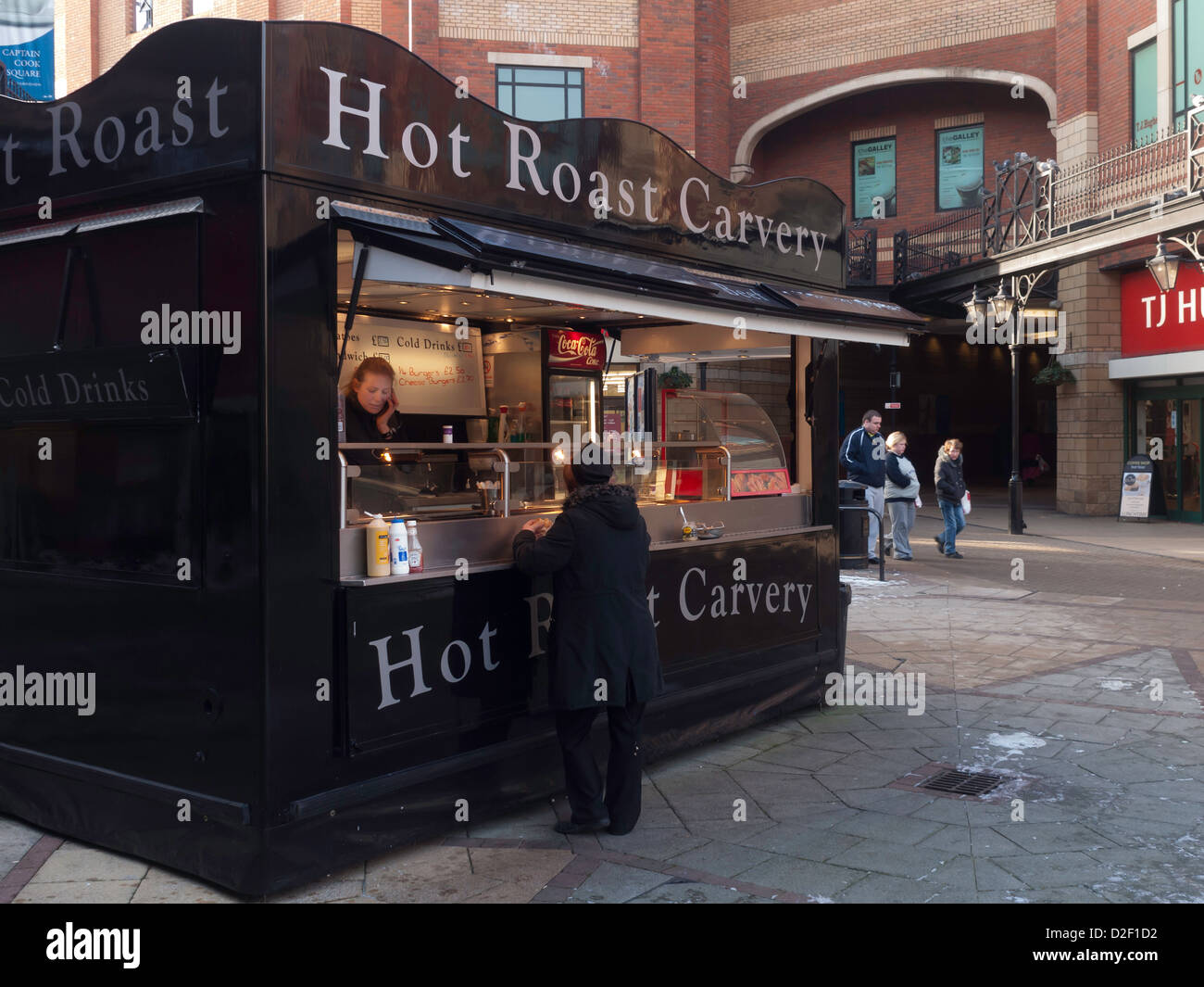 Comfort food - una donna di mangiare un burgher a caldo buffet di carni arrosto di stallo in James Cook Square Middlesbrough in una fredda giornata invernale Foto Stock