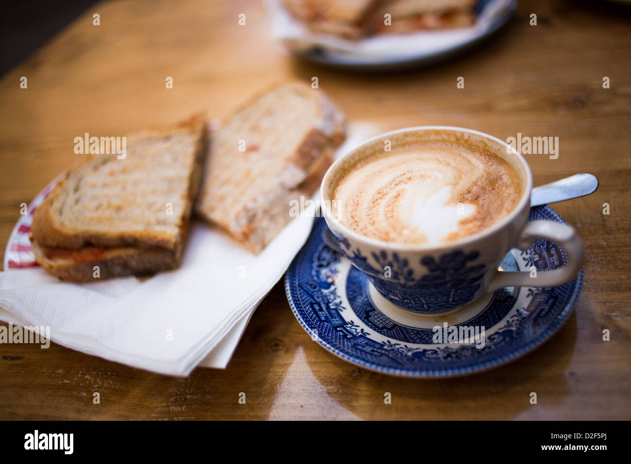 Cina tè tazza piena di caffè fresco in un piatto bianco o latte di stile con un sandwich tostato in background su un tavolo di legno. Foto Stock
