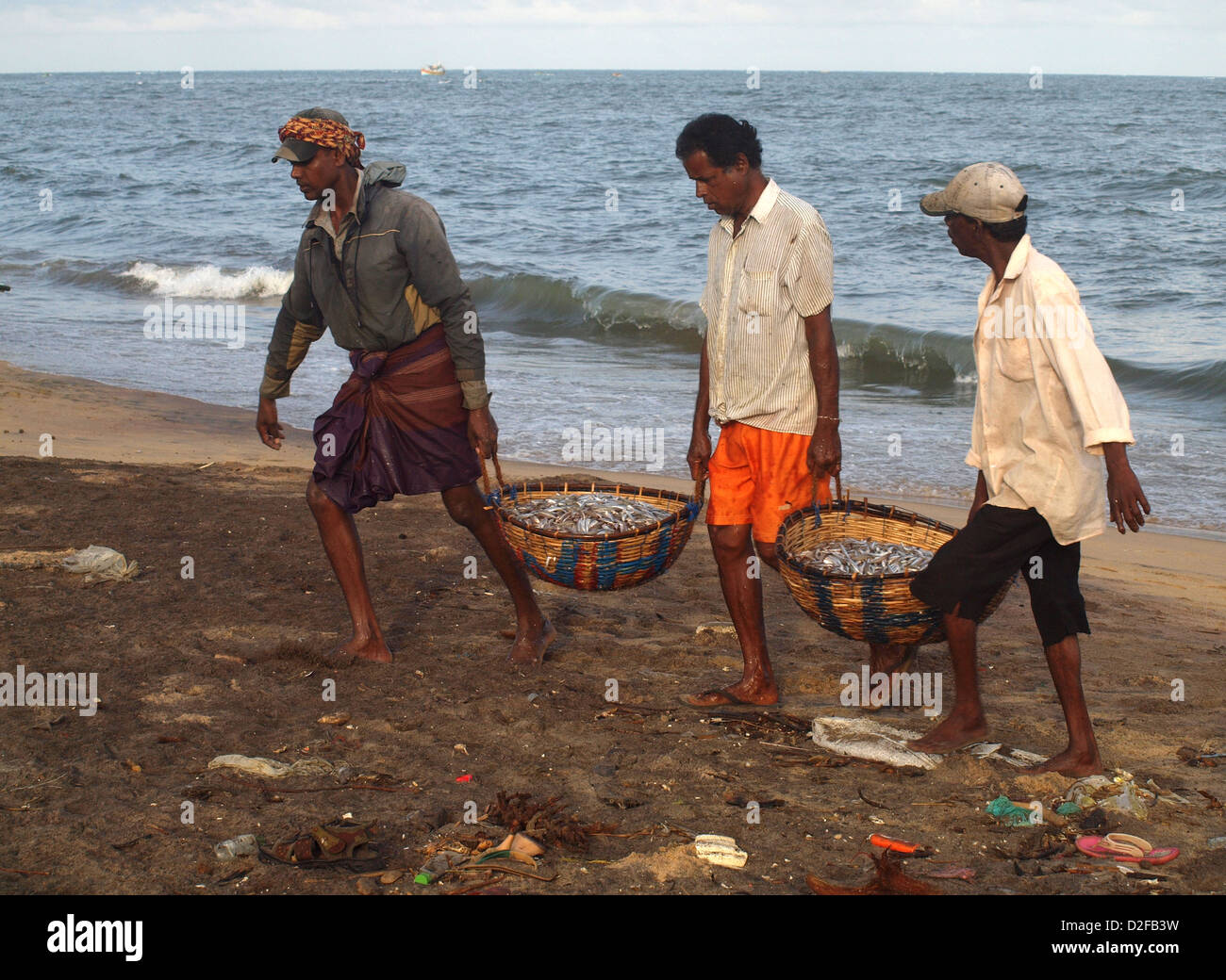 I pescatori a Negombo Sri Lanka portano ceste di pesce fino l'immondizia disseminata beach Foto Stock