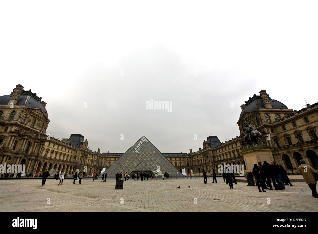 L'iconica piramide di vetro del Museo del Louvre circondata da architettura storica in una giornata nuvolosa a Parigi, in Francia Foto Stock