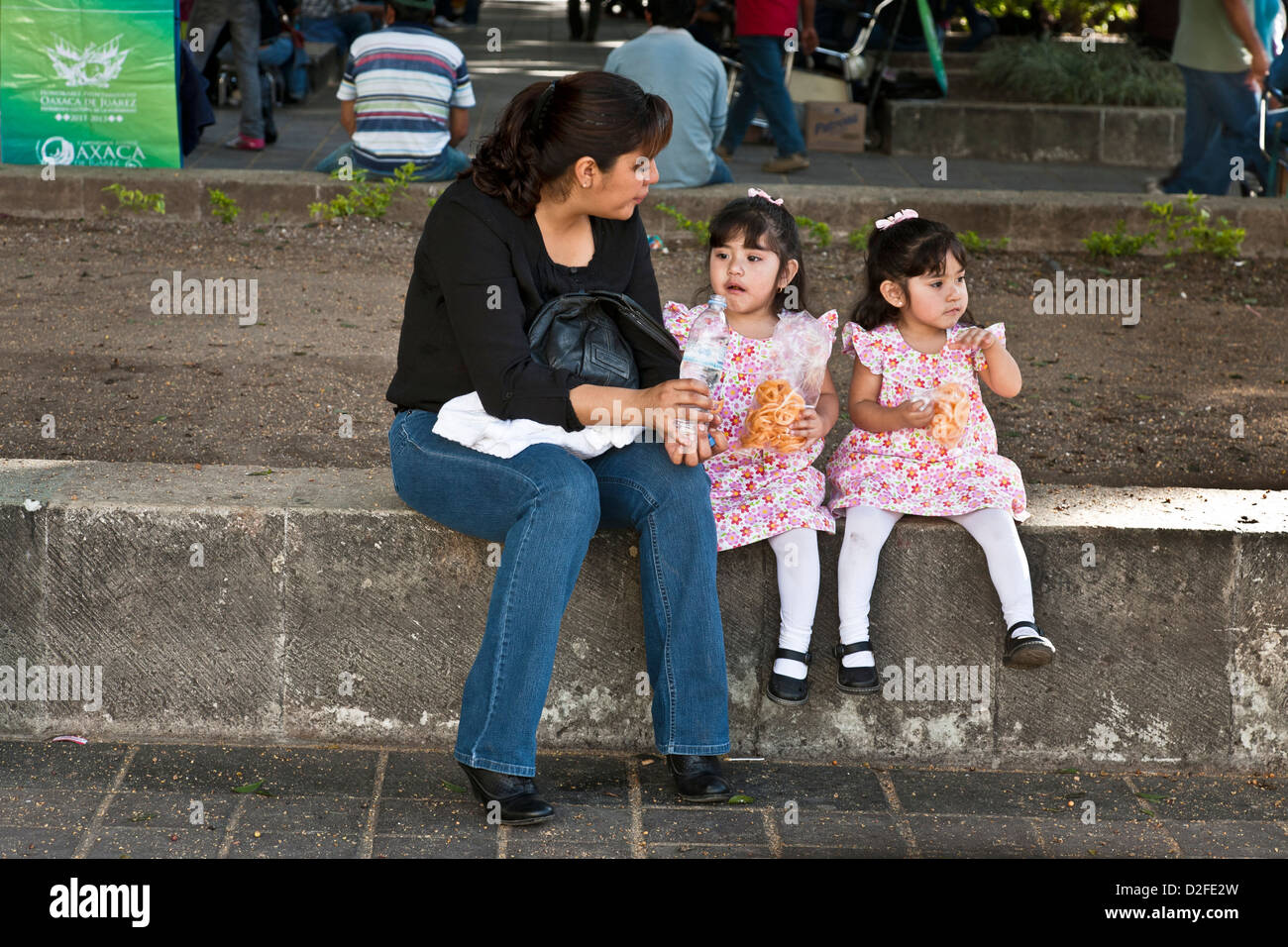 Madre messicana con piccole figlie gemelle simili vestito in abiti fioriti calze bianche & Mary janes sedersi sulla parete bassa Oaxaca Foto Stock