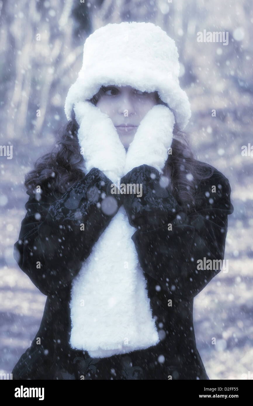 Una donna con un mantello nero, bianco guanti, sciarpa e cappello al di fuori durante la nevicata Foto Stock