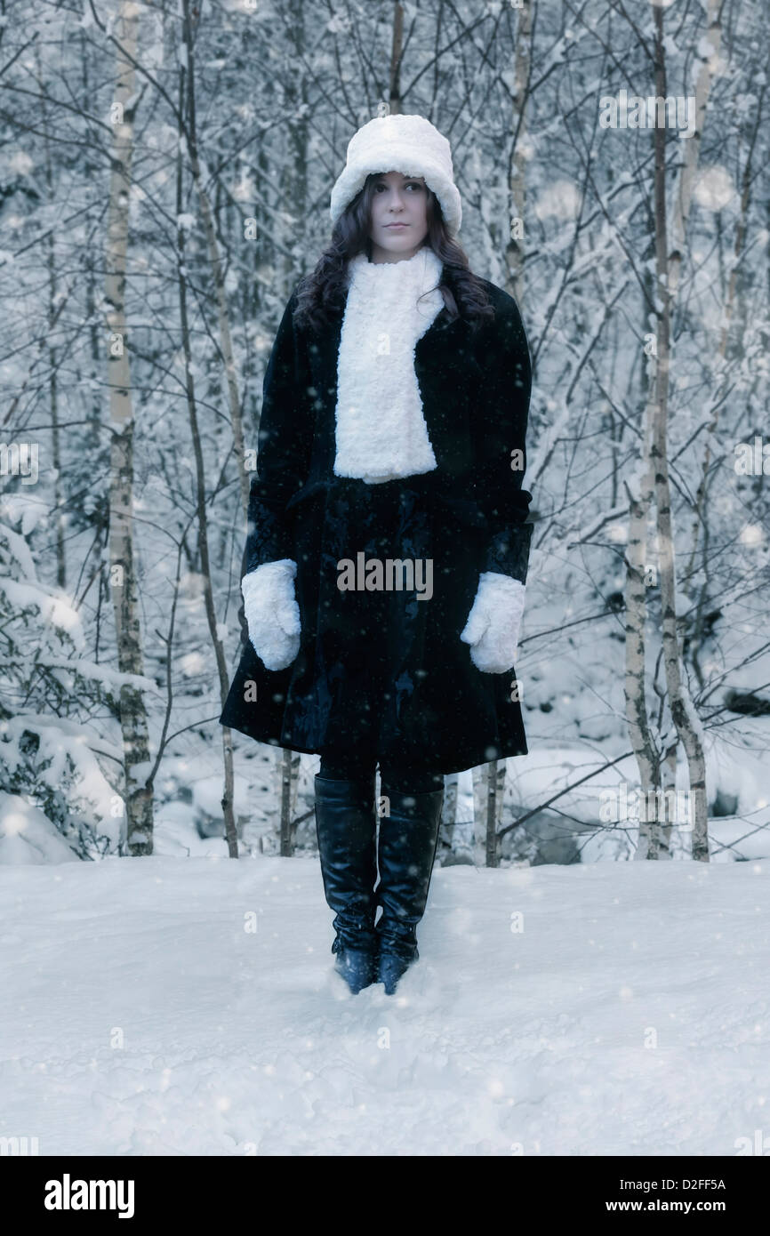 Una donna in un mantello nero con un cappello bianco e sciarpa bianco nella neve Foto Stock