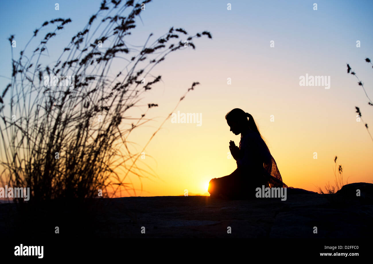 Indian ragazza adolescente pregando al tramonto nella campagna indiana. Silhouette. India Foto Stock