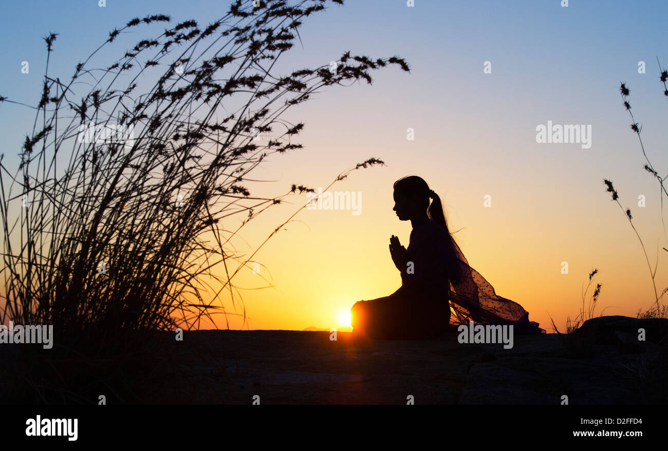 Indian ragazza adolescente pregando al tramonto nella campagna indiana. Silhouette. India Foto Stock