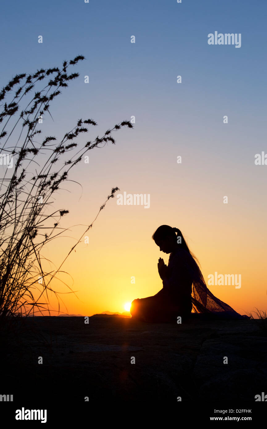 Indian ragazza adolescente pregando al tramonto nella campagna indiana. Silhouette Foto Stock