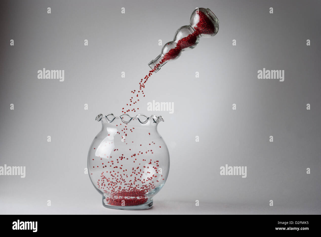 Perline rosso versando da un levitato vetro singolo a vaso in uno più grande Foto Stock