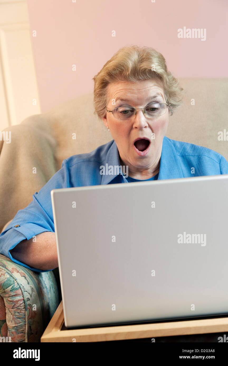 Senior Donna che utilizza il suo computer portatile con un espressione scioccato Foto Stock