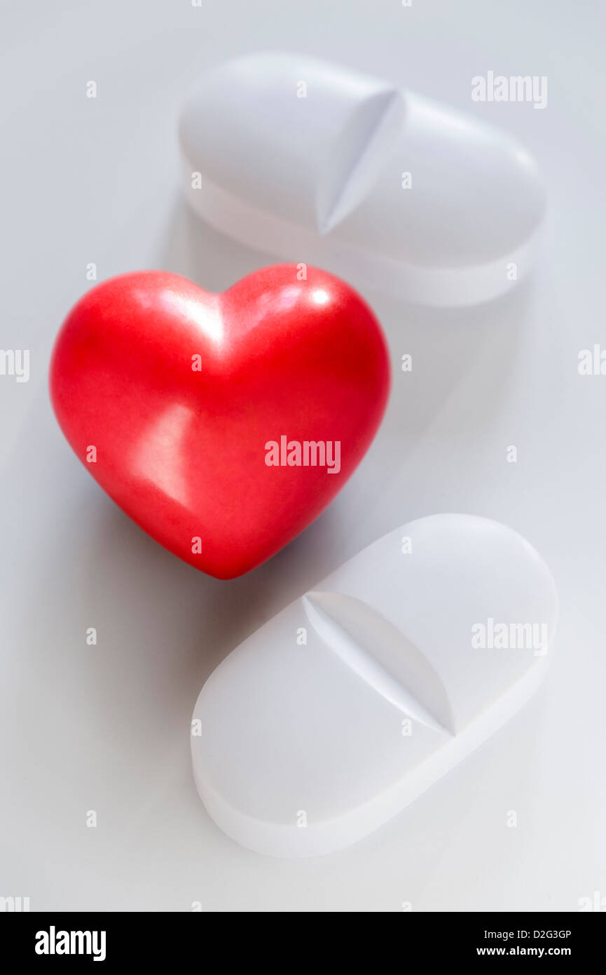Due pillole di bianco e un cuore rosso su sfondo bianco Foto Stock
