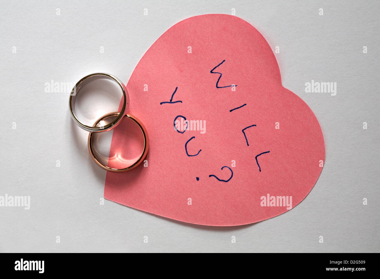 Sarà lei? Messaggio scritto sul rosa a forma di cuore post it pad con due anelli di nozze - proposta di matrimonio isolati su sfondo bianco Foto Stock