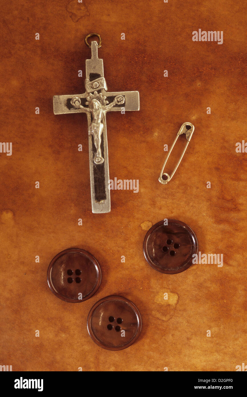 Piccolo argento e nero crocifisso giacente sul bordo con la spina di sicurezza e il marrone tre pulsanti di rivestimento Foto Stock