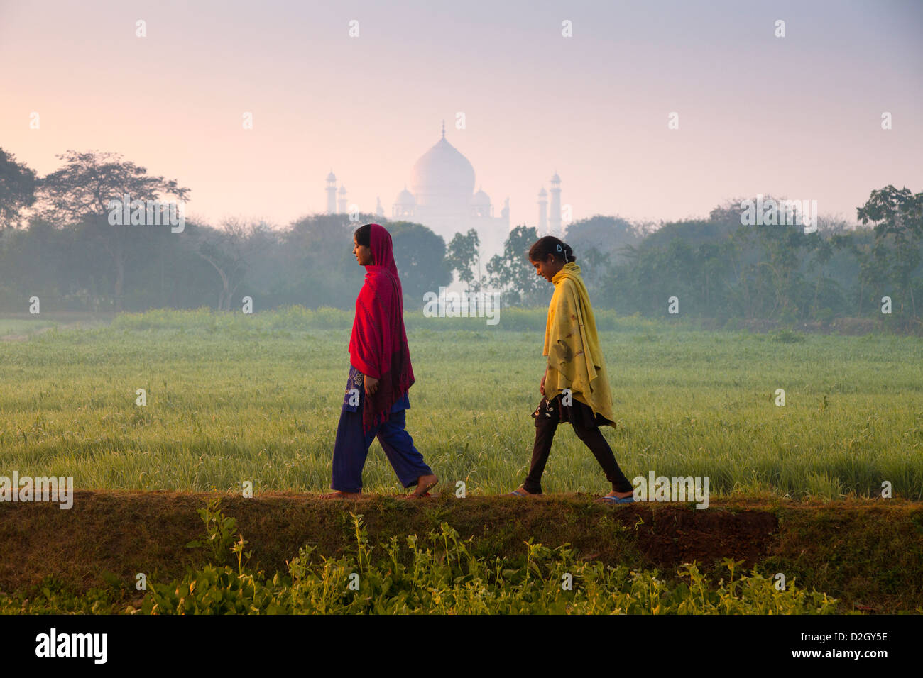 India, Uttar Pradesh, Agra due ragazze camminare attraverso il campo con Taj Mahal al di là Foto Stock