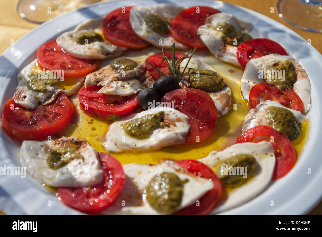 Un piatto tradizionale di pomodori, olive e mozzarella servita con olio d'oliva e basilico. Foto Stock