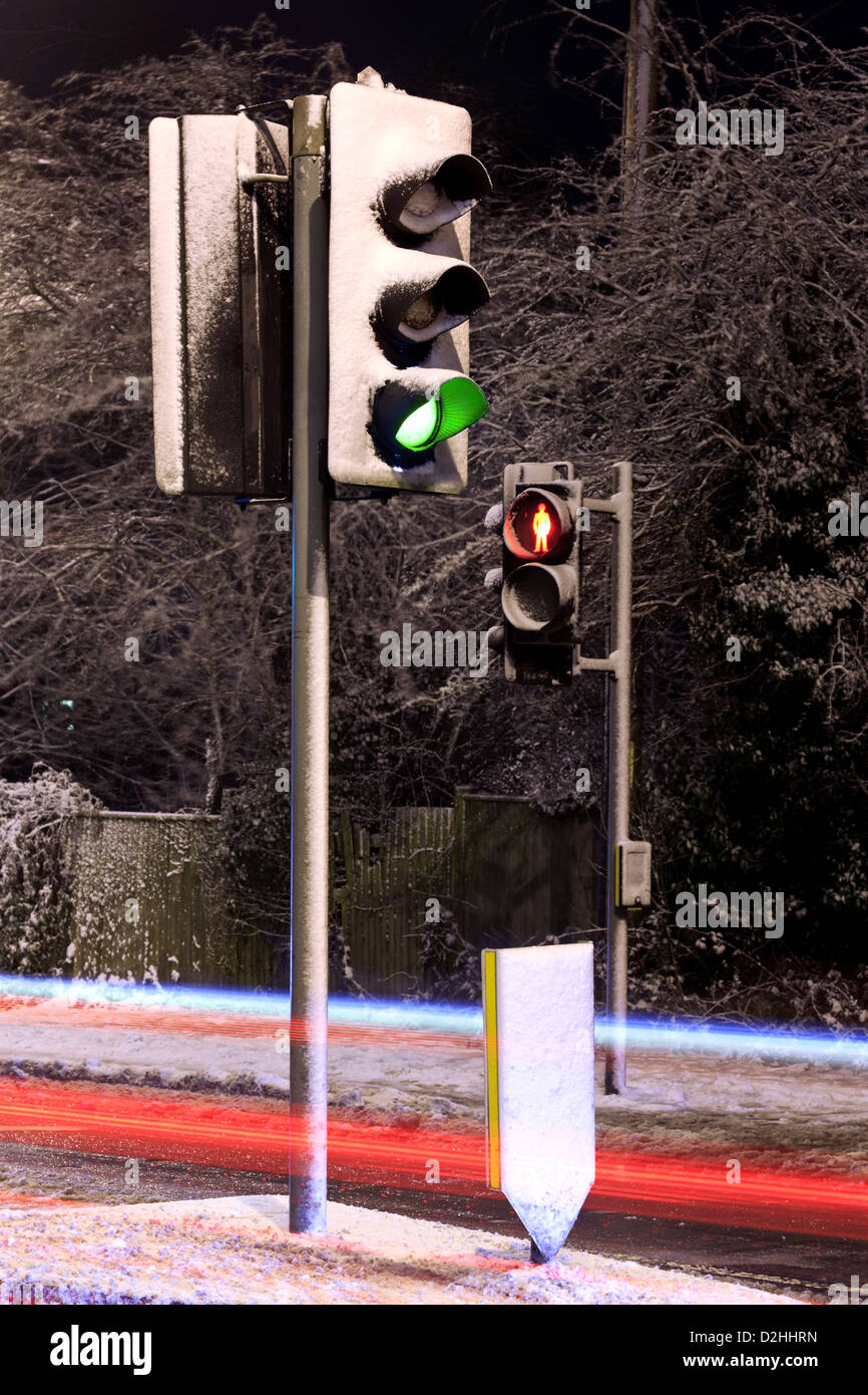 Semaforo ricoperta di neve su una strada del Regno Unito durante la notte con una luce percorsi dai veicoli in transito. Foto Stock