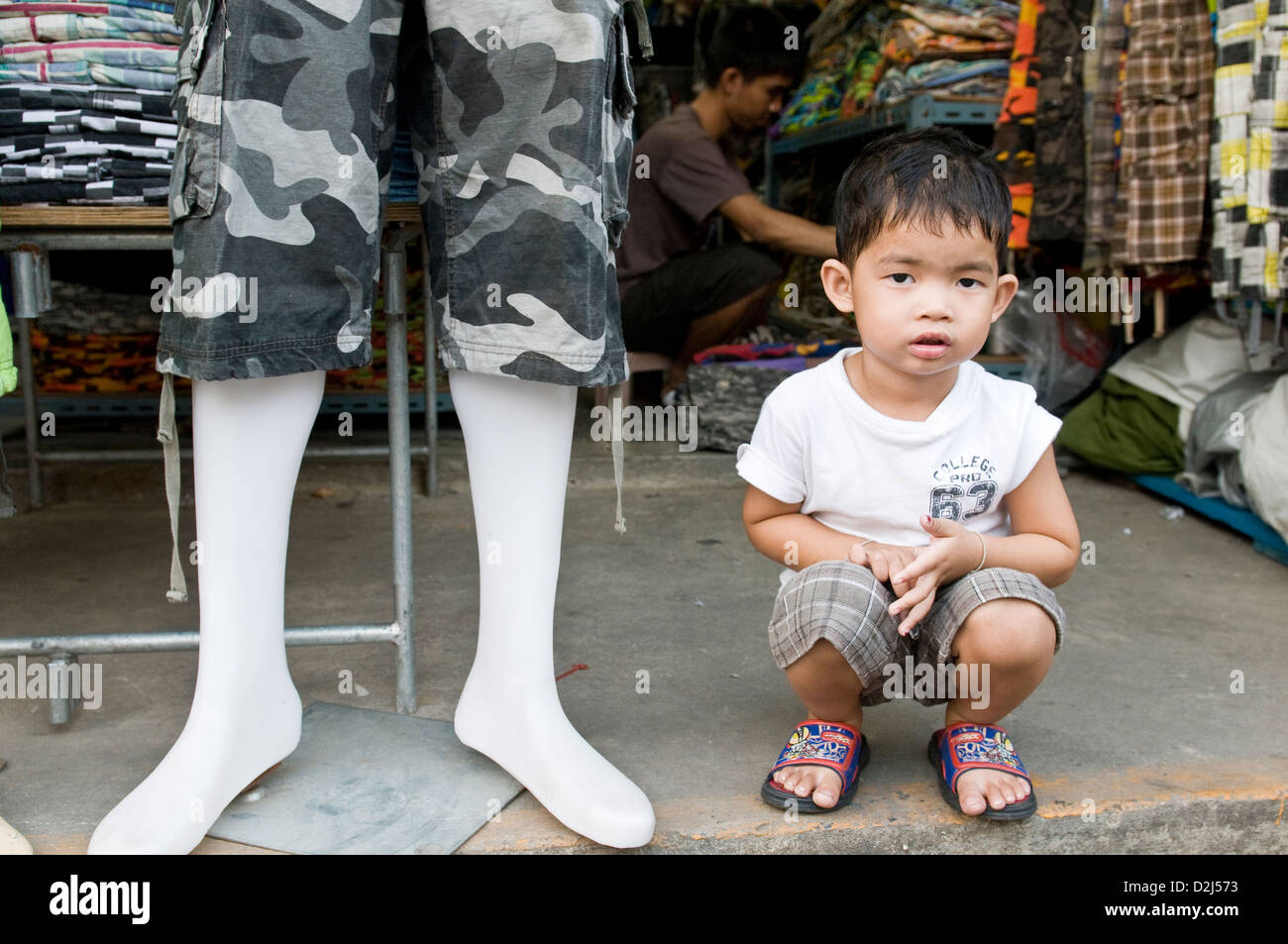 Bangkok, Thailandia, un piccolo ragazzo si siede di fronte al negozio di tessuti del padre Foto Stock