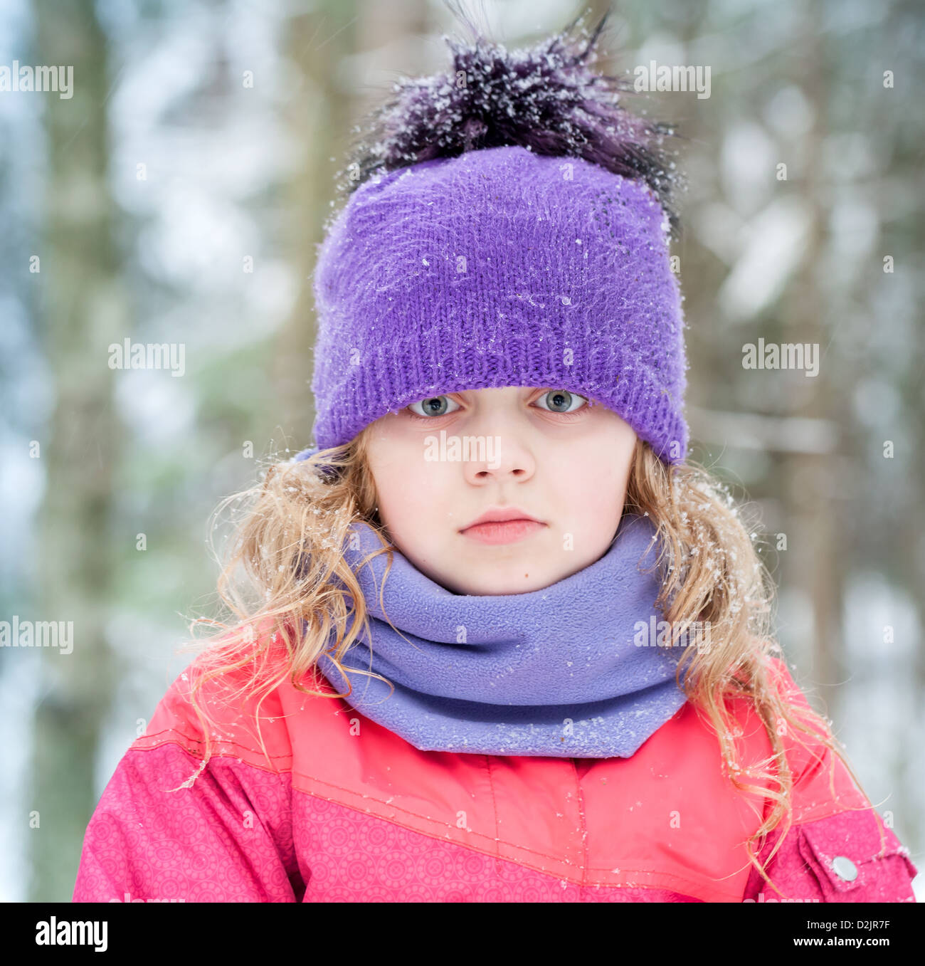 Bimba bionda in inverno abbigliamento esterno con i fiocchi di neve sopra lo sfondo di foresta Foto Stock