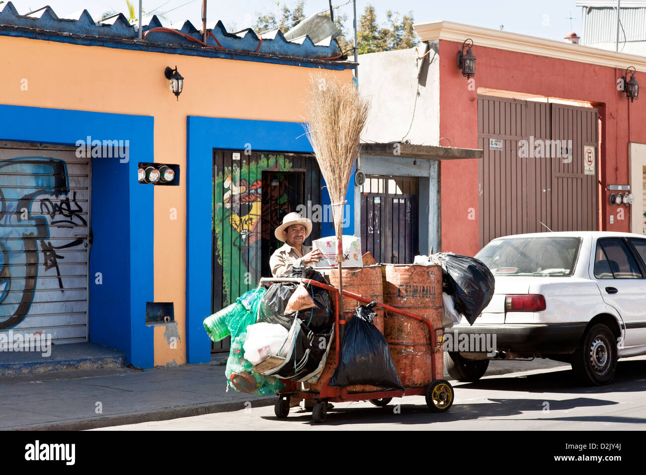 Mexican spazzatrice con impugnatura lunga scopa di paglia & recyclables appeso sul lato del carrello di fronte gli edifici colorati Oaxaca Foto Stock
