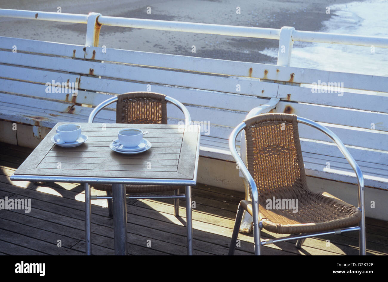 Due chrome e plastica sedie di vimini presso il cafe tabelle vuote con tazze e piattini e vista della spiaggia al di là Foto Stock