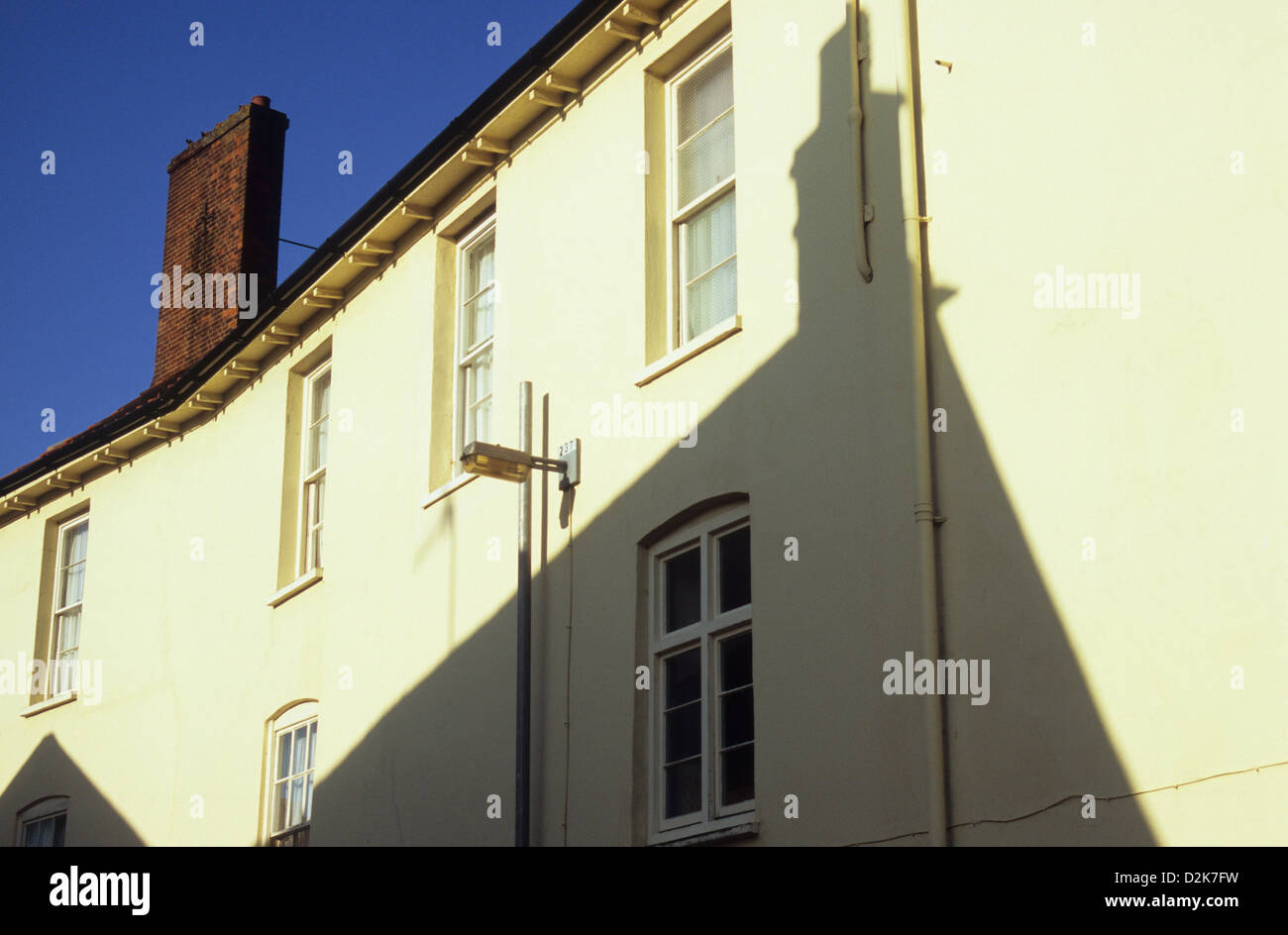 Fila di case a schiera, dipinto di bianco con un grande camino in mattoni sotto il cielo blu e l'ombra della casa di fronte Foto Stock