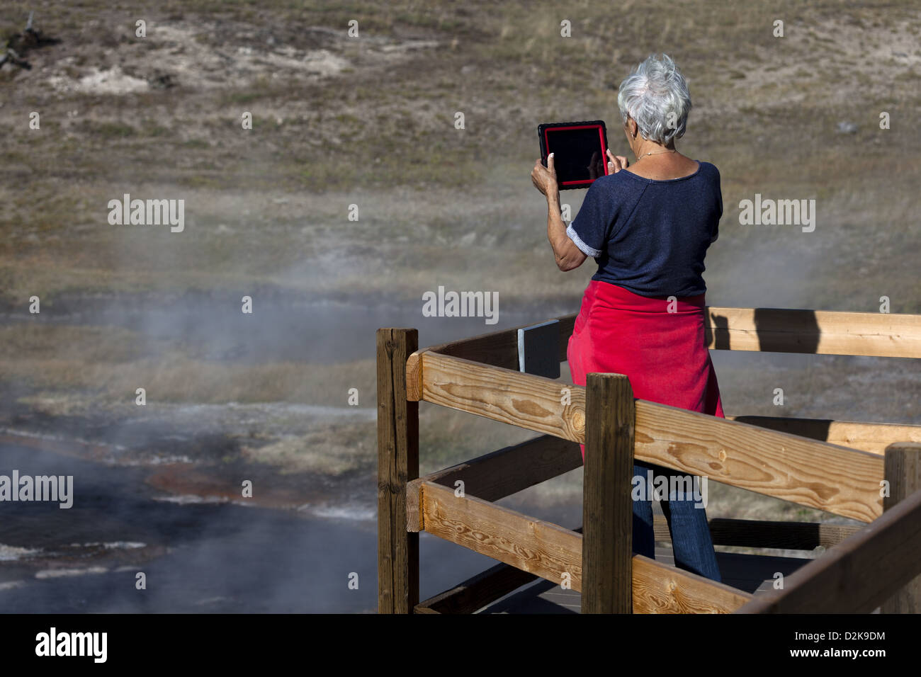 Senior Woman su un vialetto in legno che fotografa Yellowstone, utilizzando un tablet iPad Foto Stock