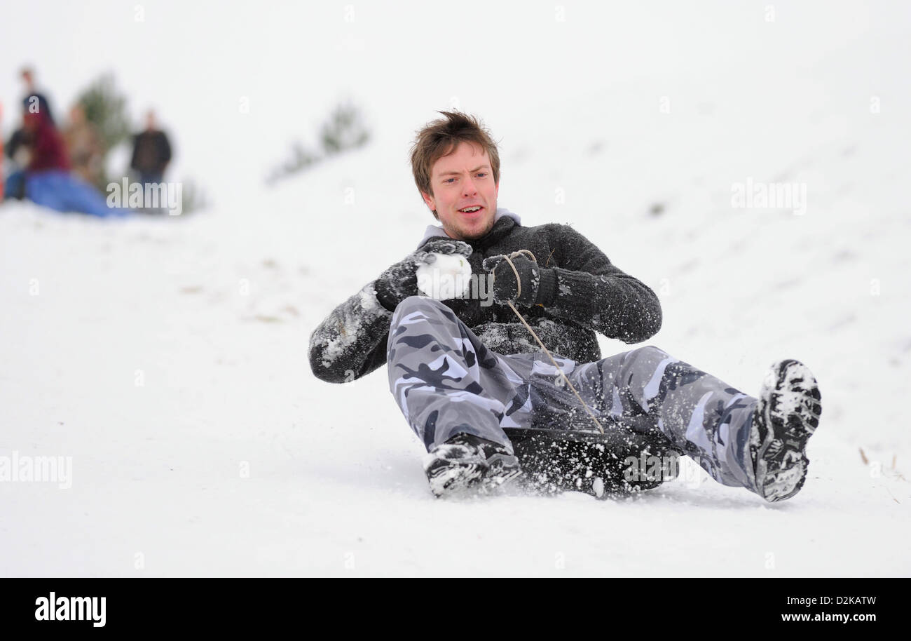 Giovani uomini godendo di slittare verso il basso una coperta di neve collina su un inverni freddi giorno. Foto Stock