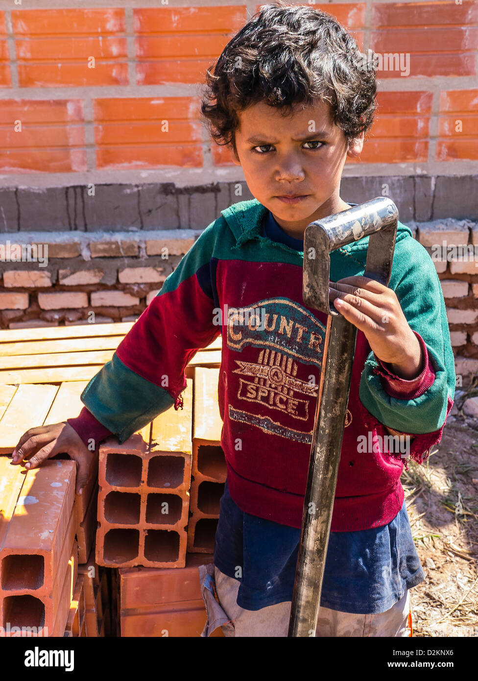 Un giovane ragazzo in Paraguay tenendo la sua mano su una pala e fissando attentamente dritto in un Habitat for Humanity sito di costruzione Foto Stock