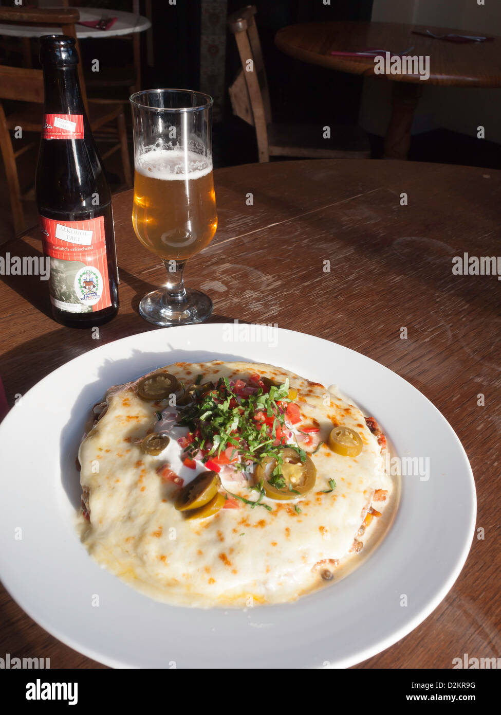 Il pranzo di lenticchie piccante tortilla integrale con il formaggio fuso di panna acida salsa jalapeños e con un bicchiere di alcool liberi lager Foto Stock