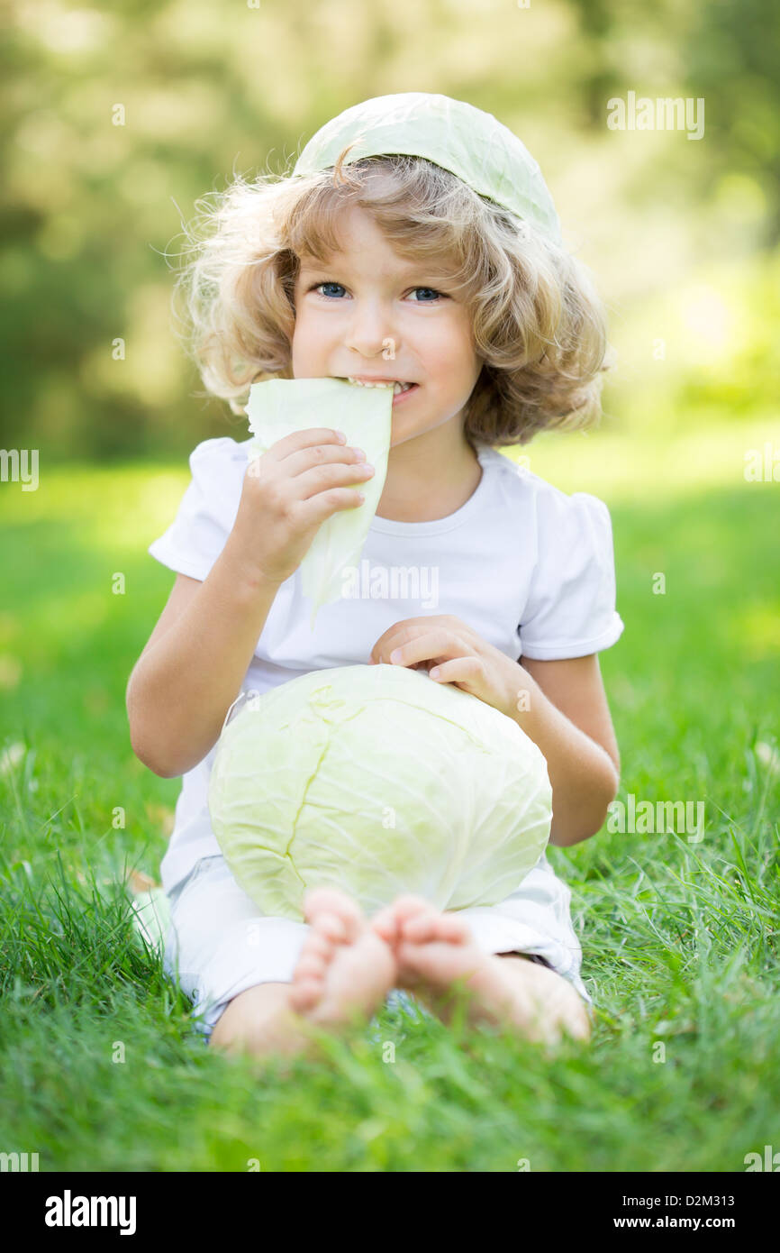 Bambino contento di mangiare il cavolo verde contro lo sfondo della molla Foto Stock